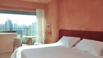 Camera d'albergo con un letto, un tavolino e una sedia. Una finestra offre vista sulla città.
