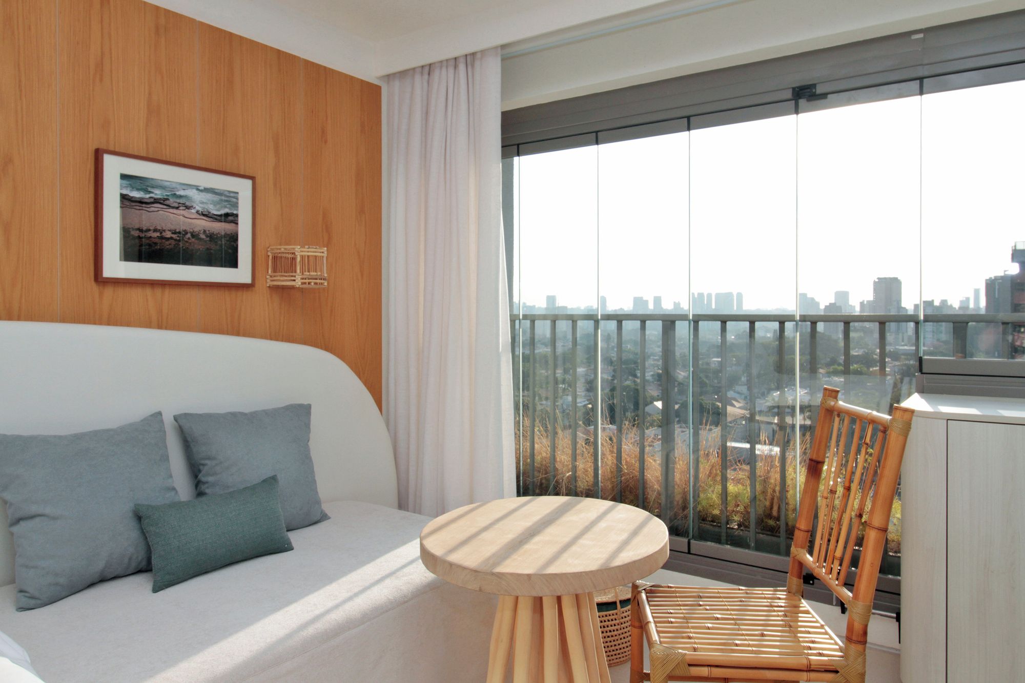 Une chambre d’hôtel moderne avec un balcon, un canapé avec des coussins, une table ronde en bois et une chaise.
