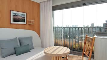 A modern hotel room with a balcony, a sofa with cushions, a round wooden table, and a chair.
