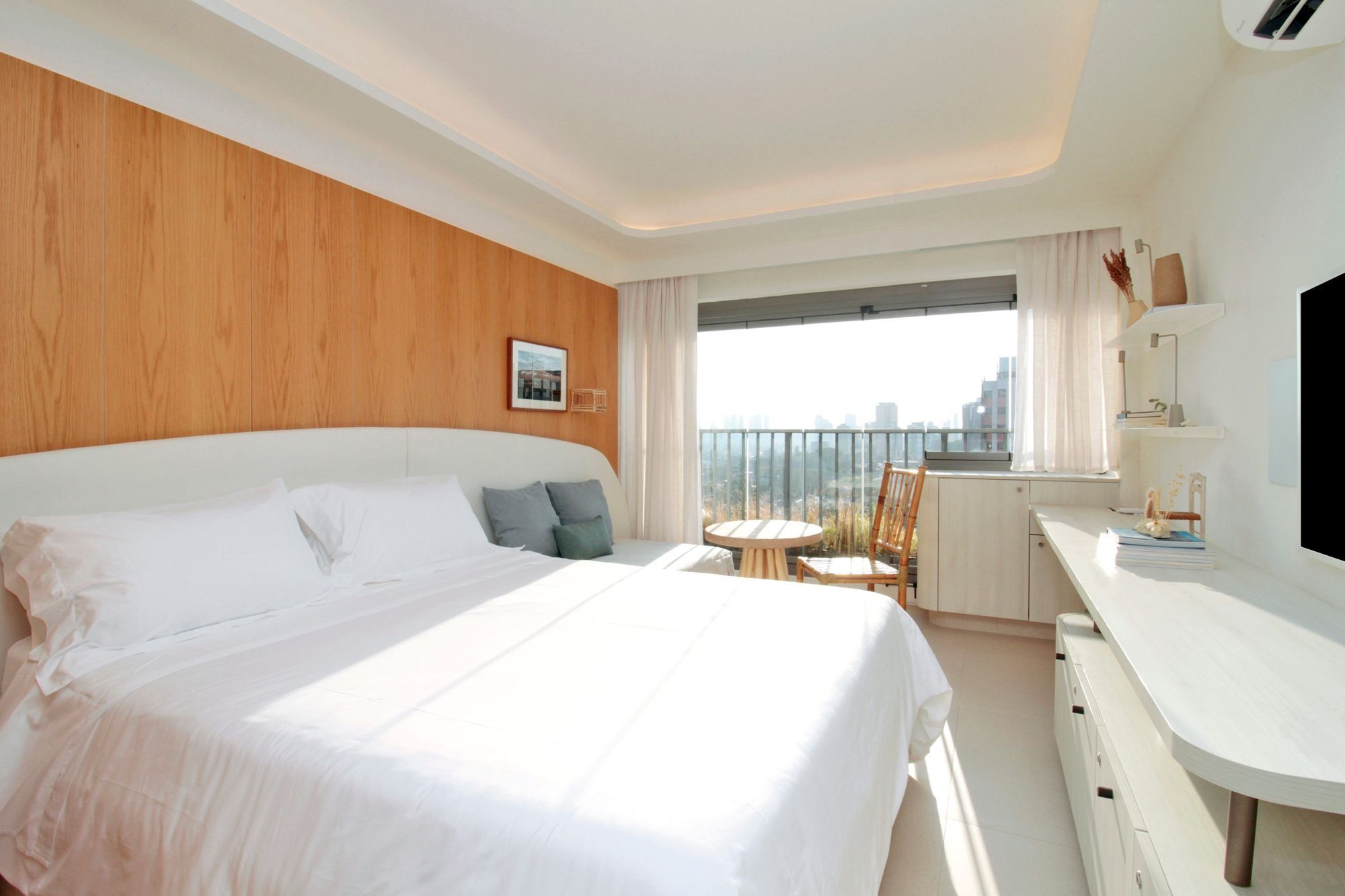 A hotel room with a large bed, a desk, a chair, a small table, and a view of the city.