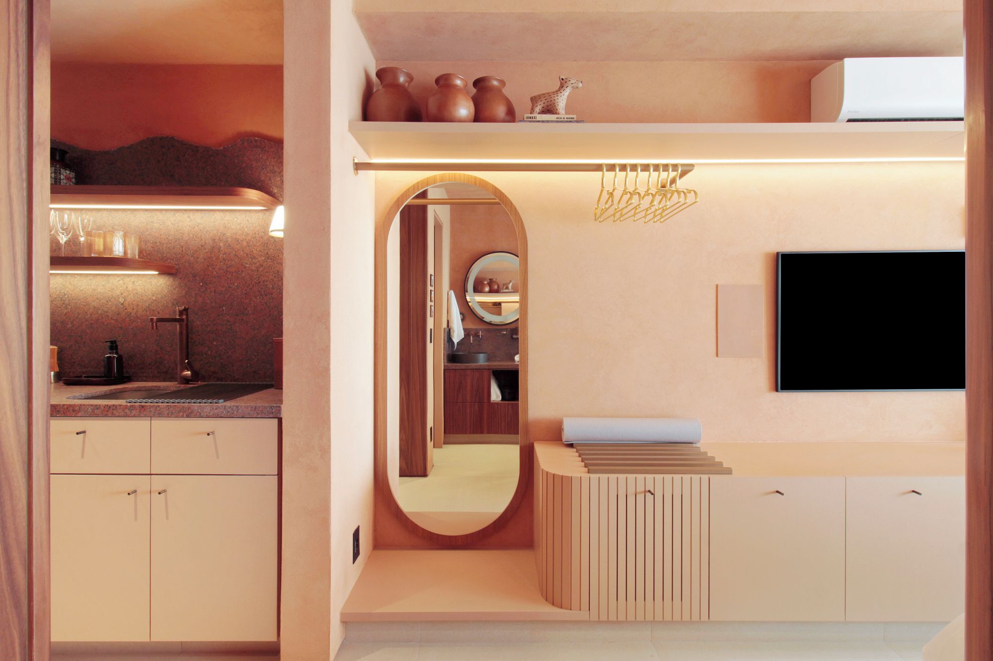 A modern bathroom with a vanity, mirror, and a flat-screen TV mounted on the wall.