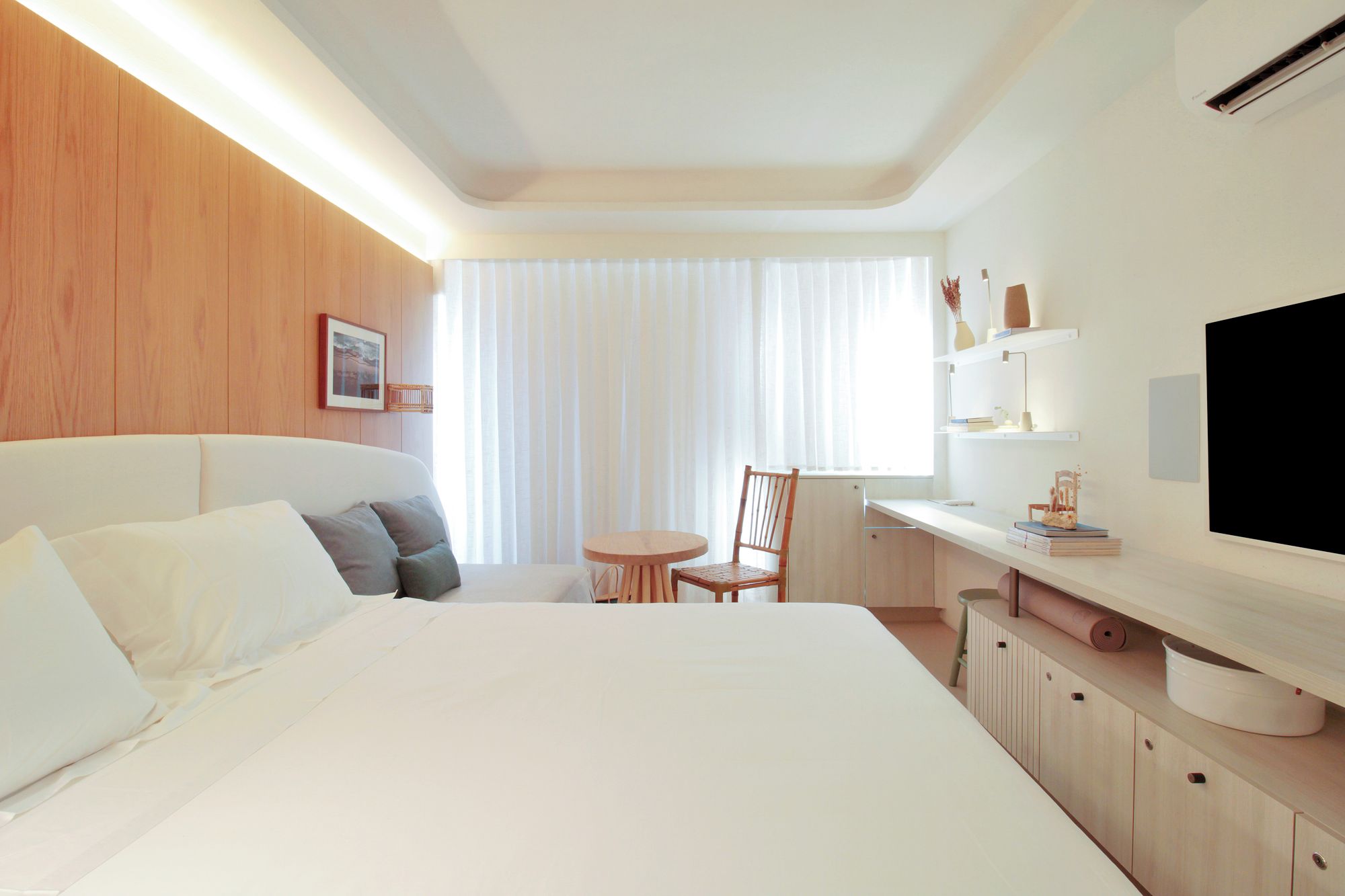 Quarto de hotel com cama, escrivaninha, cadeira, televisão e janela com cortinas.