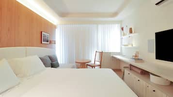 Quarto de hotel com cama, escrivaninha, cadeira, televisão e janela com cortinas.