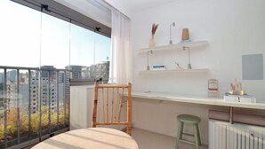Un apartamento moderno con un ventanal grande, una silla de madera, un taburete pequeño, un escritorio blanco y un radiador.