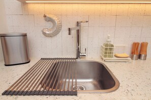 A kitchen with a stainless steel sink, a soap dispenser, and a trash can. - MOBE Studios (São Paulo)