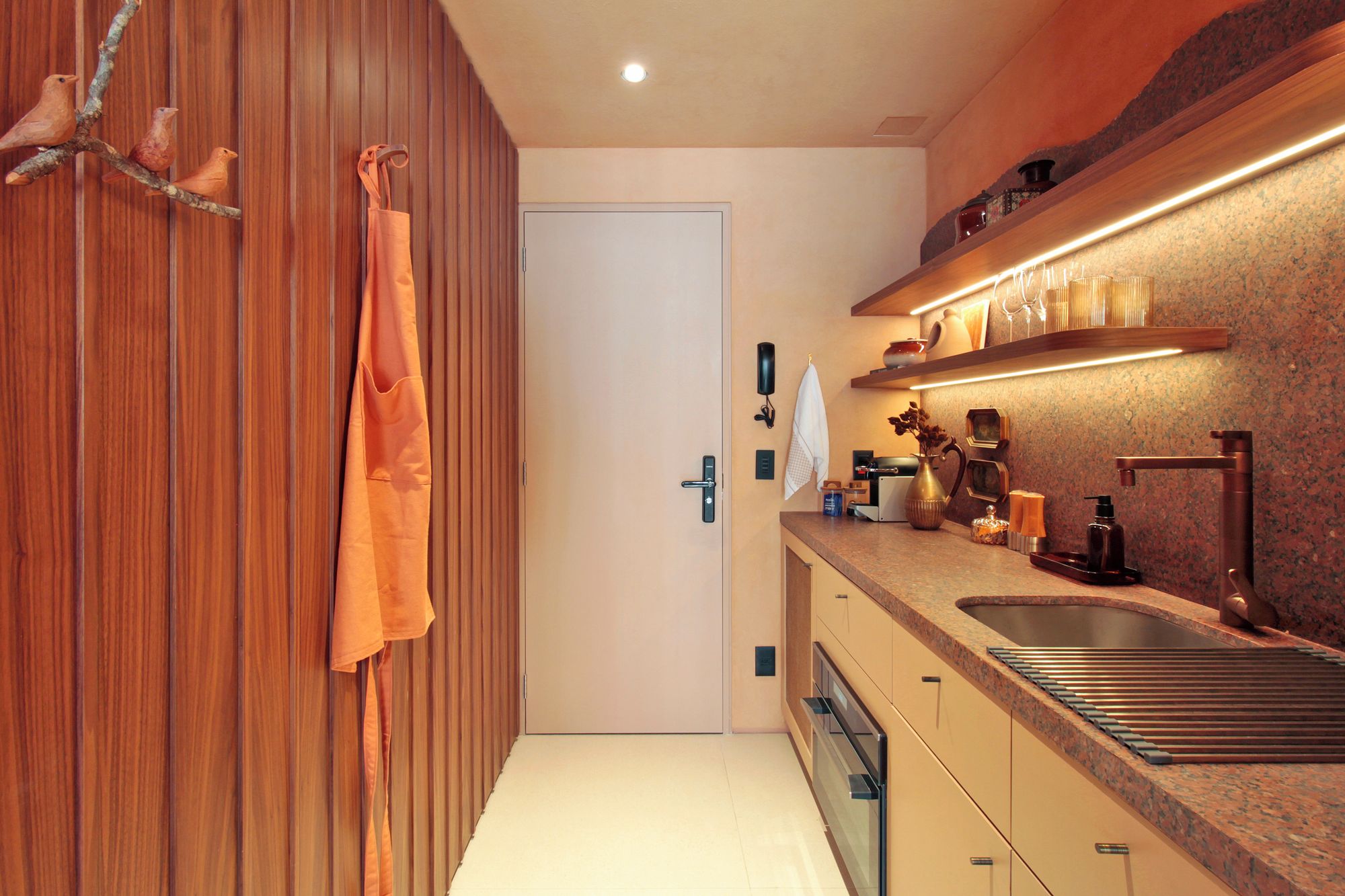 Una cocina moderna con horno integrado, lavamanos y encimera con varios electrodomésticos.
