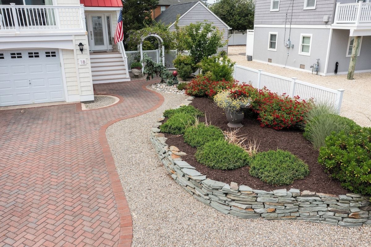 A residential property with a brick driveway, a stone border garden, and a white fence.