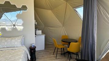 A tent-style room with a bed, a small kitchenette, and a dining area with yellow chairs.