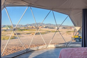 A tent with a view of a desert landscape, mountains, and a parking area with vehicles.