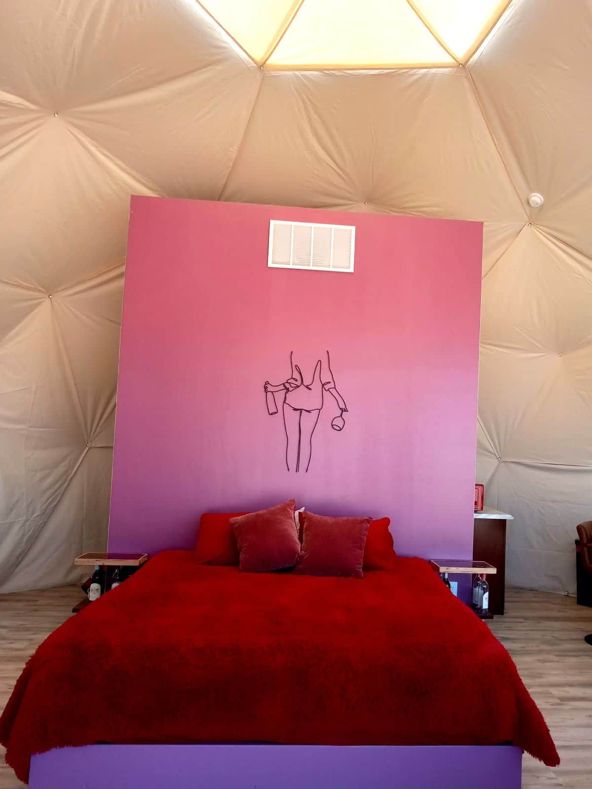 A tented room with a bed, a wall with a pink panel, and a small window.