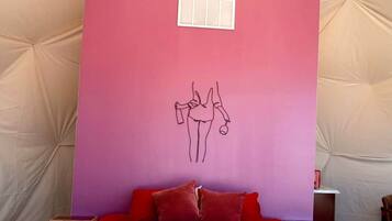 A tented room with a bed, a wall with a pink panel, and a small window.