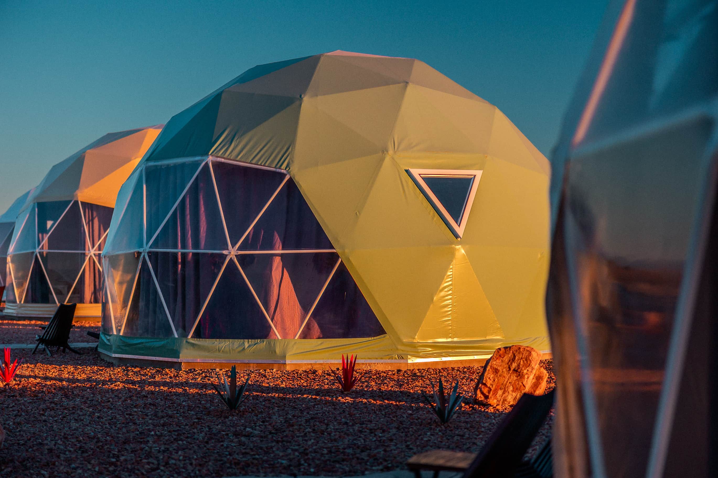 A series of geodesic dome structures with triangular windows, arranged in a row on a gravel surface.