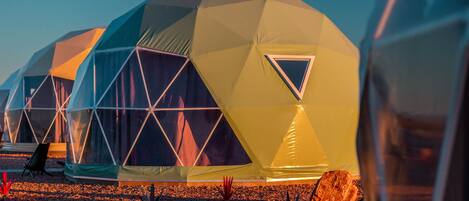 Una serie de estructuras en forma de domos geodésicos con ventanas triangulares, alineadas sobre una superficie de grava.