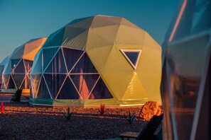 A series of geodesic dome structures with triangular windows, arranged in a row on a gravel surface. - Cowboy Dome at Tirrito Farm (Cochise County)