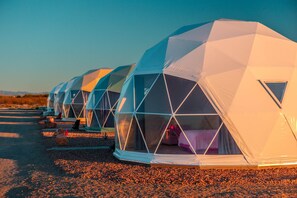 Una hilera de tiendas en forma de cúpula con entrada triangular, dispuestas sobre una superficie de grava.