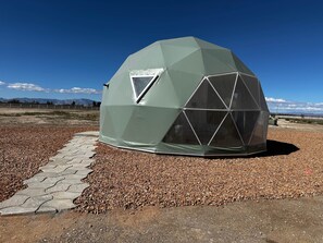 A geodesic dome structure with a triangular window, surrounded by gravel and a paved path.
