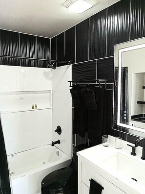 Un baño con una bañera blanca, un espejo grande y un perchero negro.