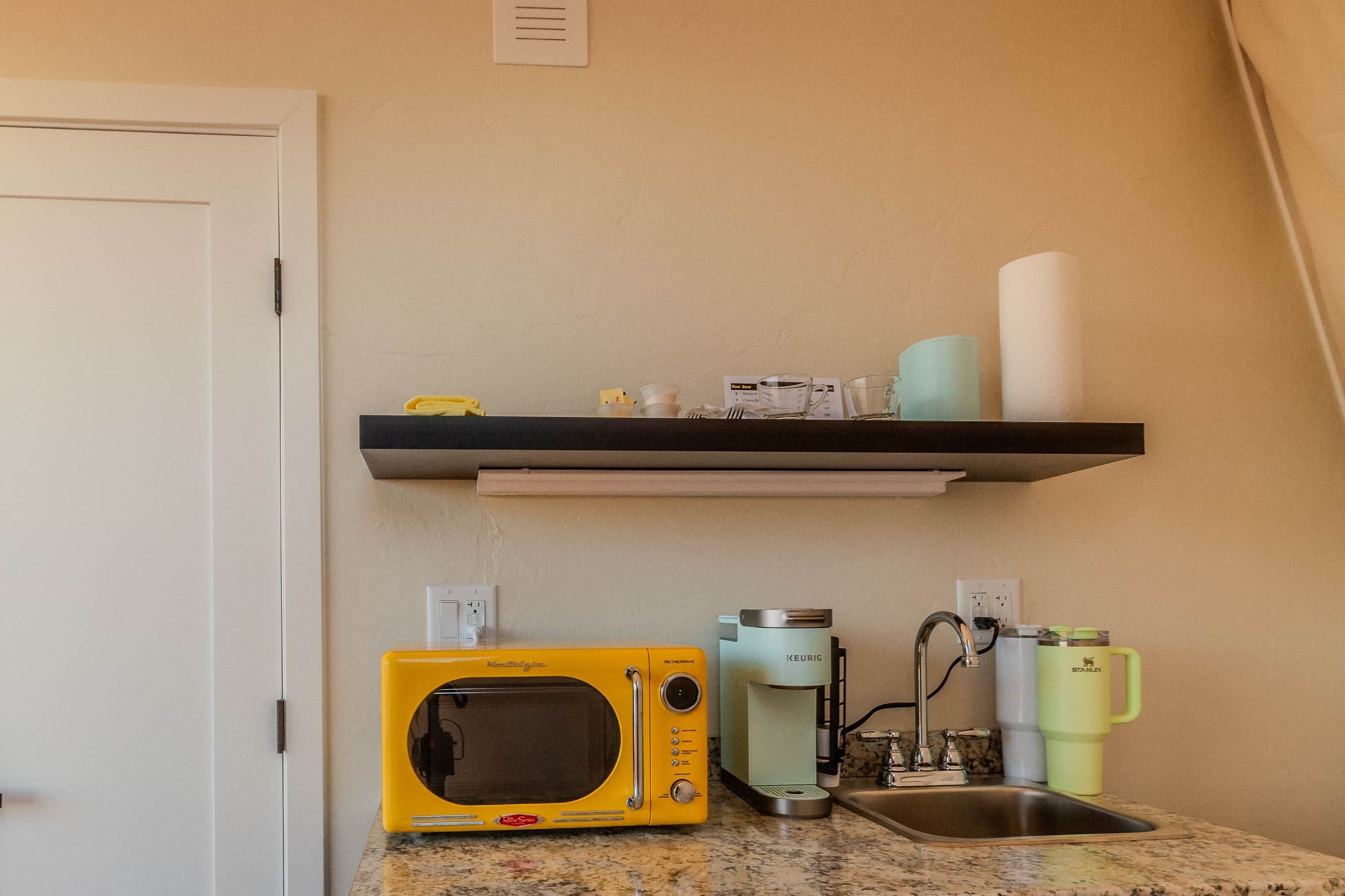 A kitchen with a microwave, coffee maker, and a shelf with kitchen items.
