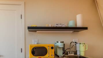 A kitchen with a microwave, coffee maker, and a shelf with kitchen items.