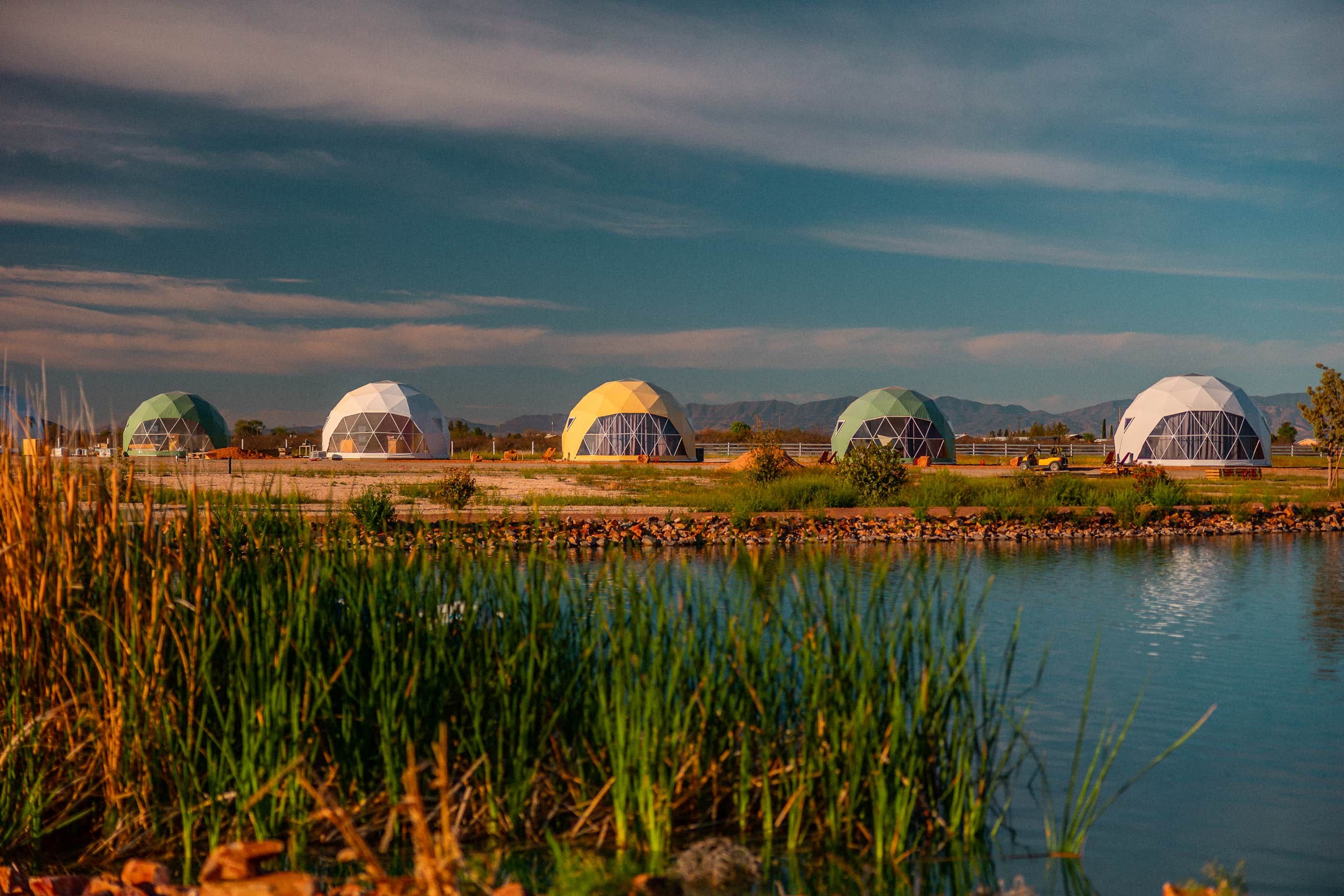 A row of geodesic dome structures by a body of water with a clear sky.