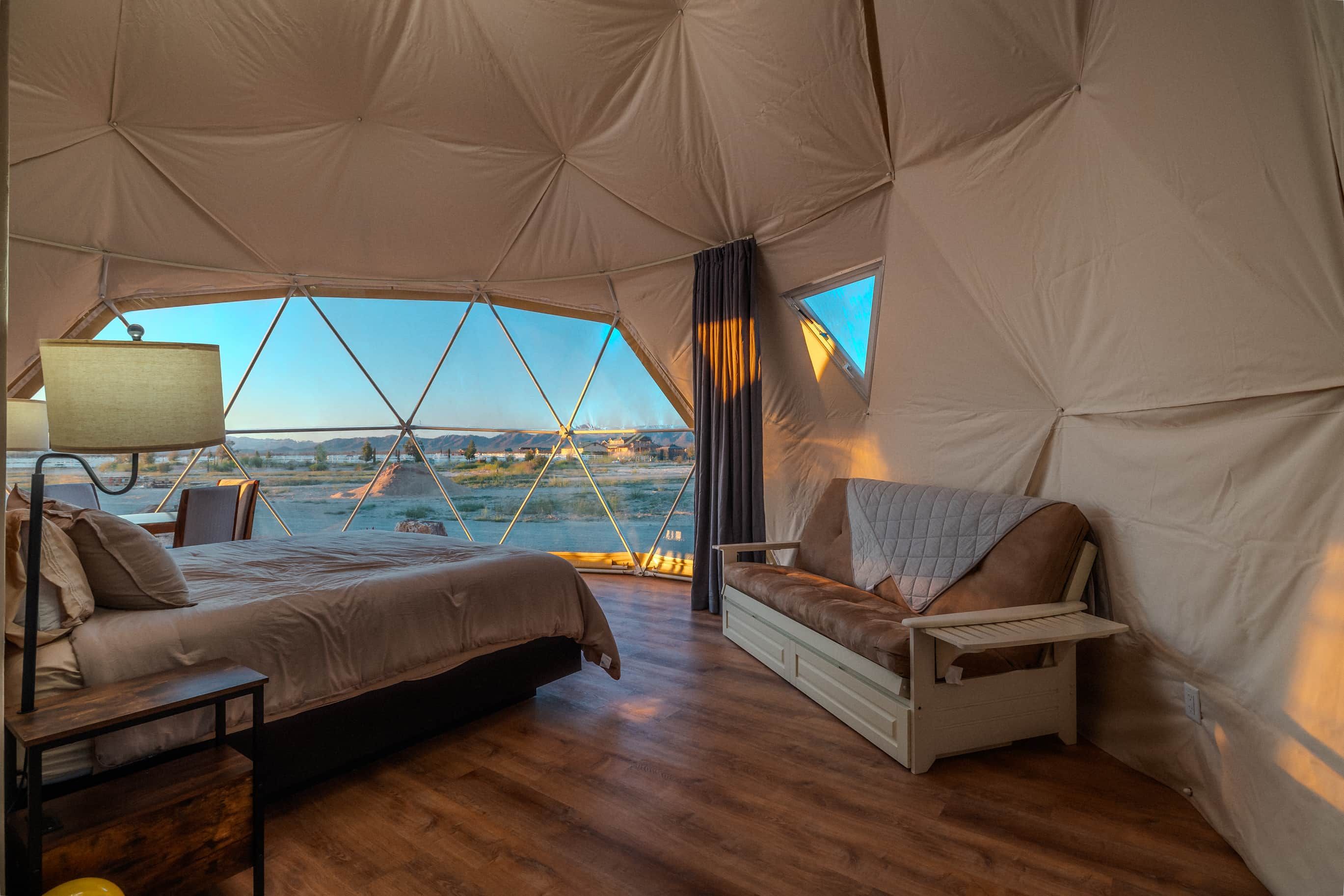 A tented accommodation with a bed, a sofa, and a table.