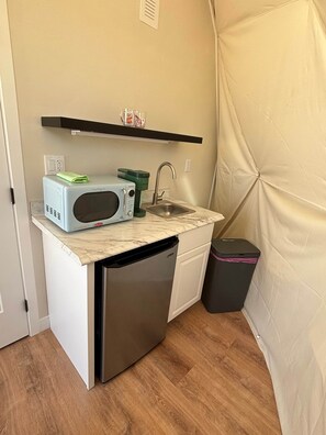 Eine kleine Küchenzeile mit Mikrowelle, Kaffeemaschine und Spüle.