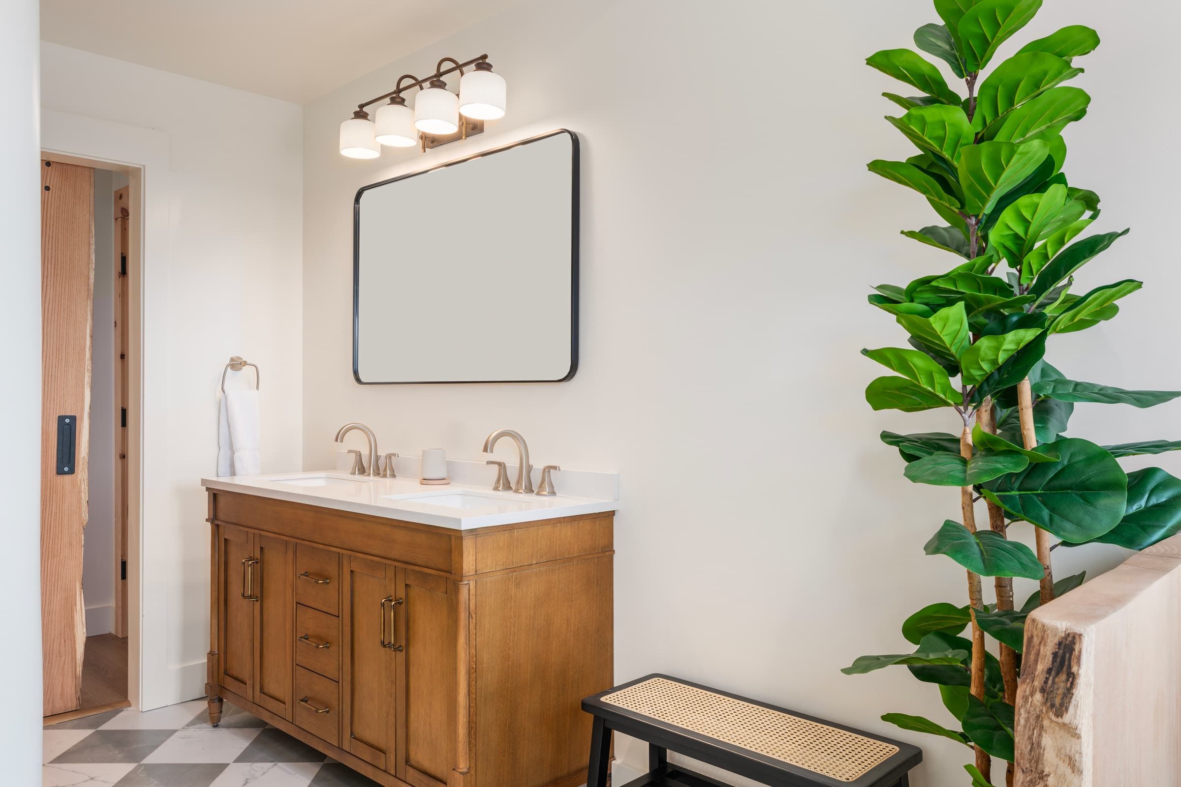 Une salle de bain avec un meuble-lavabo en bois, deux vasques, un miroir et une plante en pot.