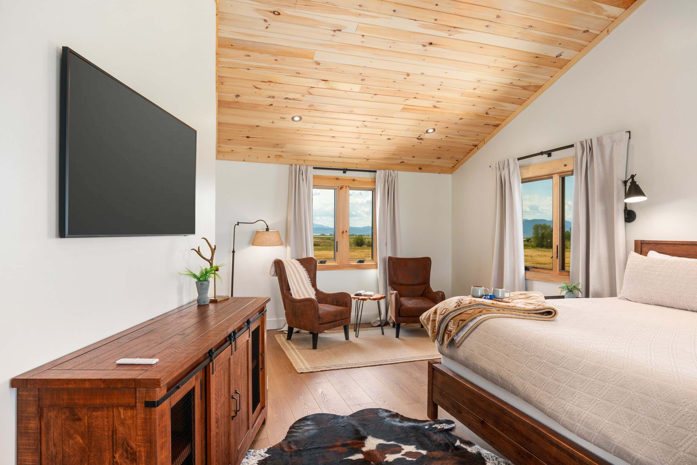 Un dormitorio con cama, escritorio, silla, lámpara y vistas al exterior.