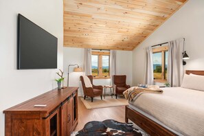 A bedroom with a bed, a desk, a chair, a lamp, and a view of the outdoors.
