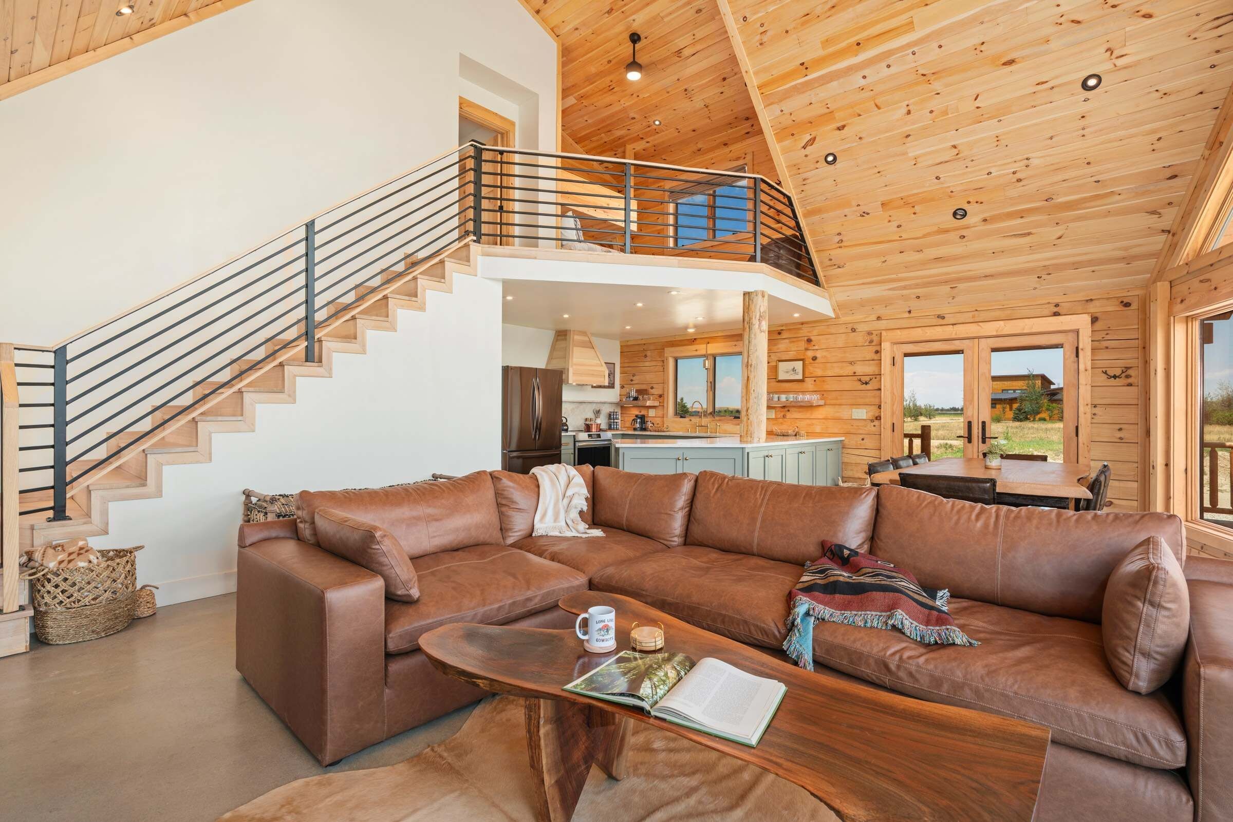 A spacious living area with a brown leather sofa, a wooden coffee table, and a staircase leading to an upper level.