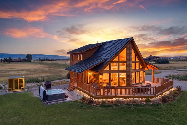 A log cabin with a deck, hot tub, and a scenic view of the landscape.