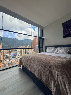 A bedroom with a large window, a bed with a brown blanket, and a cityscape view. - Tranquil 1-bedroom apartment in vibrant Bogotá D.C (Bogotá, D.C.)