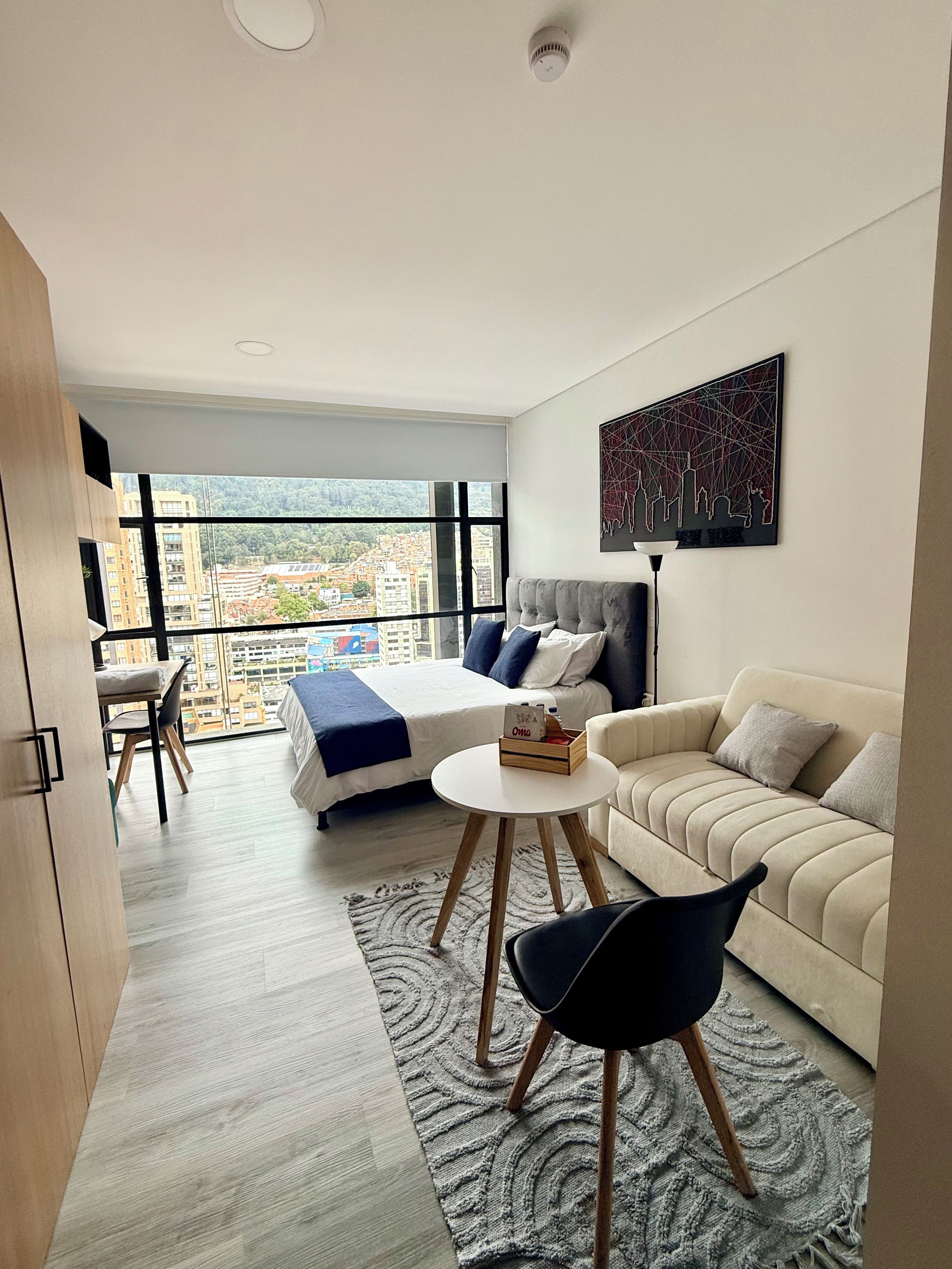 Une chambre d’hôtel moderne avec une grande fenêtre, un lit, un canapé, une petite table et une chaise.