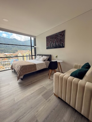 Ein modernes Schlafzimmer mit Bett, einer Couch, einem kleinen Tisch und Blick auf die Stadt.