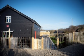 A black building with a wooden fence in front, a red door, and a sign that reads 'Secret Water.' - Secret Water is a large house with wood-burning hot tub set on a small holding. (haverfordwest)