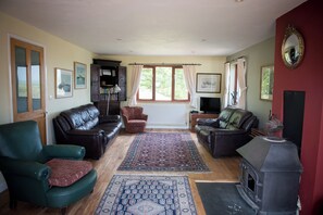 A living room with leather sofas, a fireplace, a bookshelf, and a large window with curtains. - Secret Water is a large house with wood-burning hot tub set on a small holding. (haverfordwest)