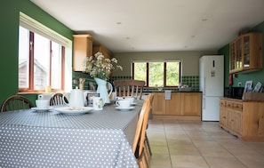 A kitchen with a dining table, chairs, a refrigerator, wooden cabinets, and a window with a view of greenery. - Secret Water is a large house with wood-burning hot tub set on a small holding. (haverfordwest)