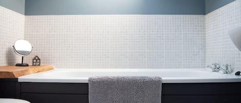 A bathroom with a bathtub, a toilet, a mirror, and a towel hanging on the wall.