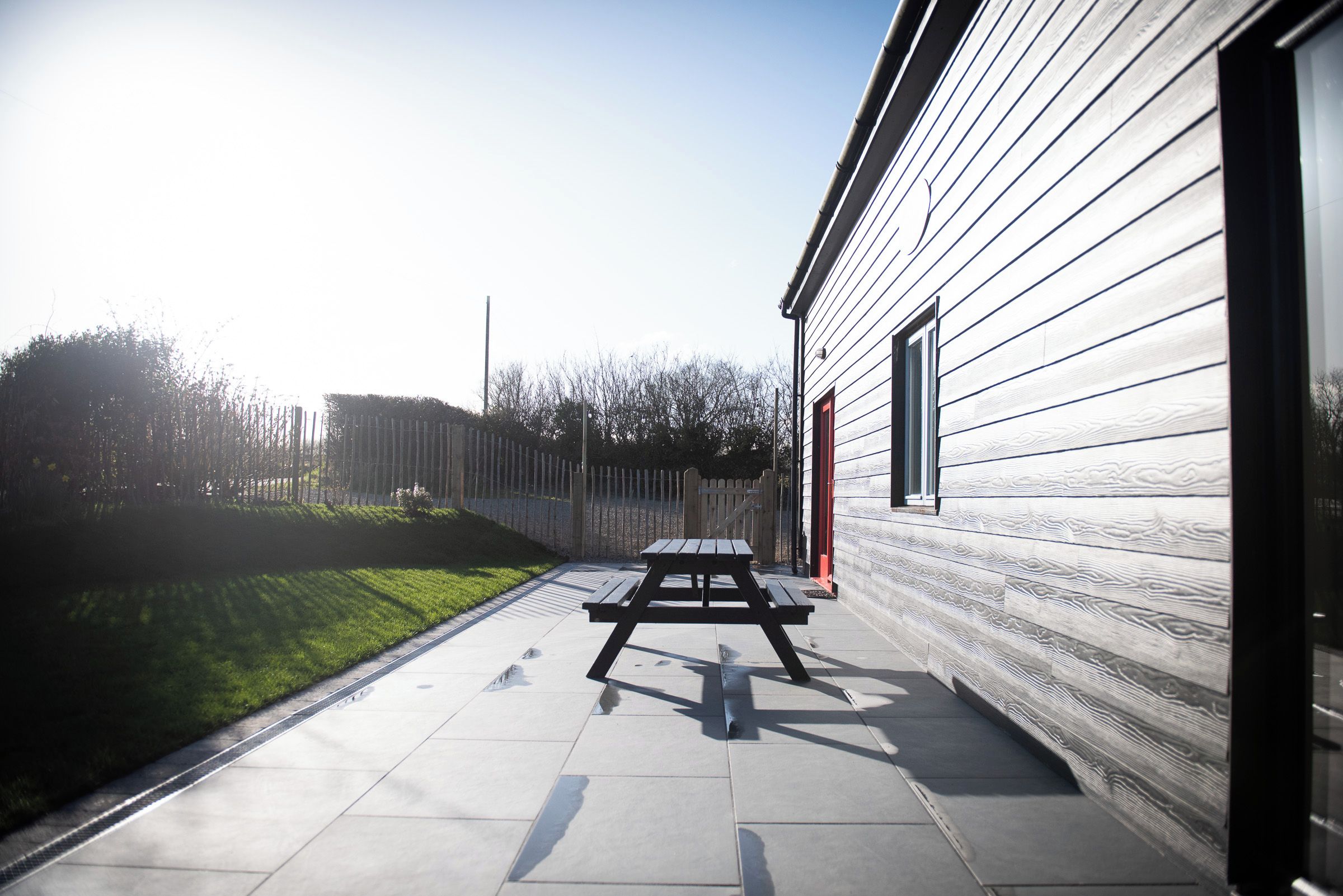 A patio area with a picnic table and a building with horizontal siding.