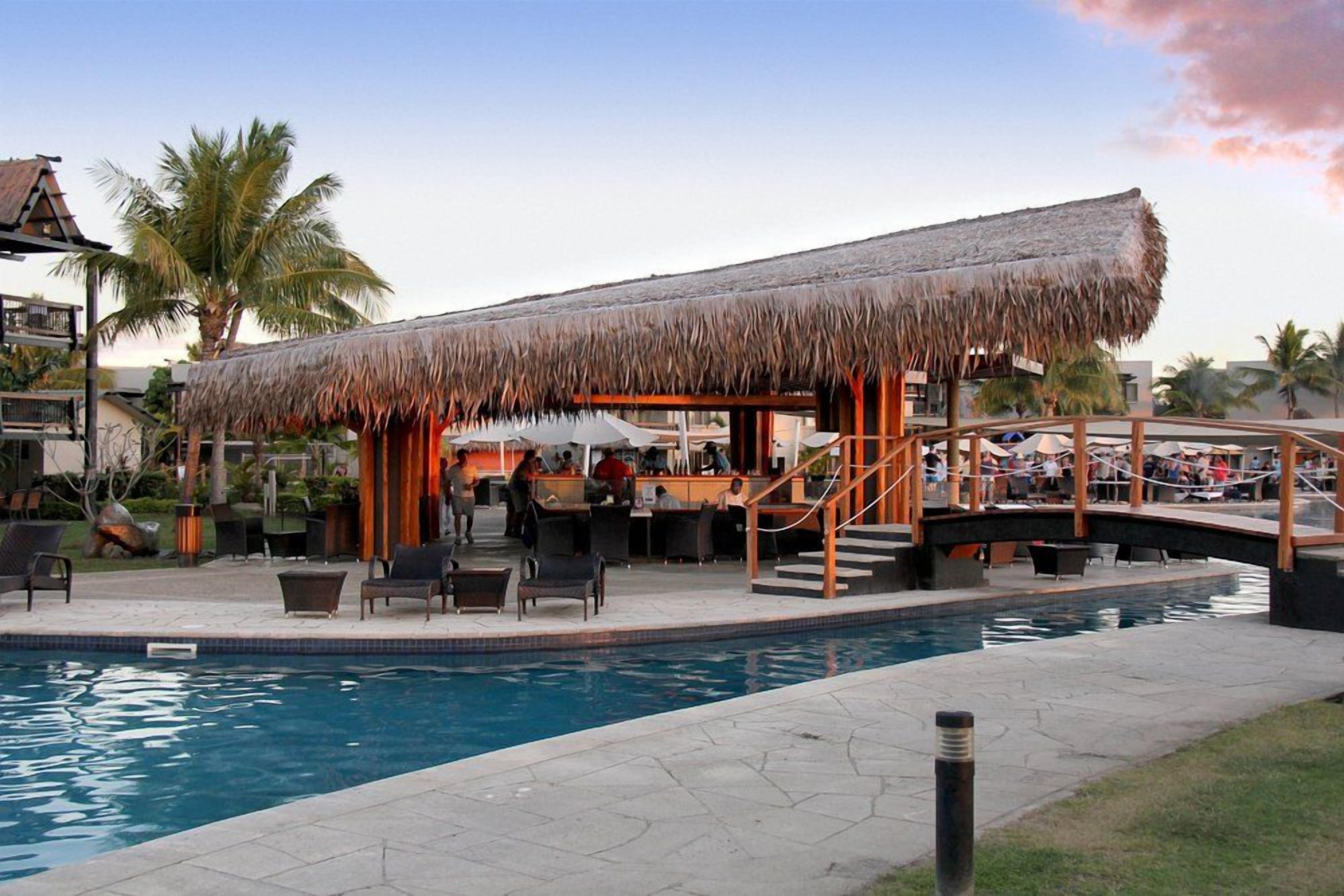 A poolside area with a thatched-roof structure, lounge chairs, and a pool.