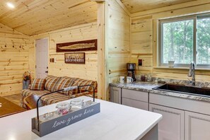 Ein Ferienhaus-Interieur mit einer Couch, einer Kaffeestation, einem Waschbecken und einem Fenster mit Blick auf Bäume.