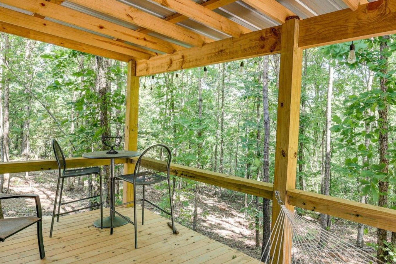 Een houten terras met een tafel en stoelen, omringd door een bos.