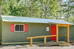 A small, single-story building with a green exterior and a red door, featuring a wooden bench and a small porch. - Boudreaux Run Cabin Ouachita National Forrest (Langley)