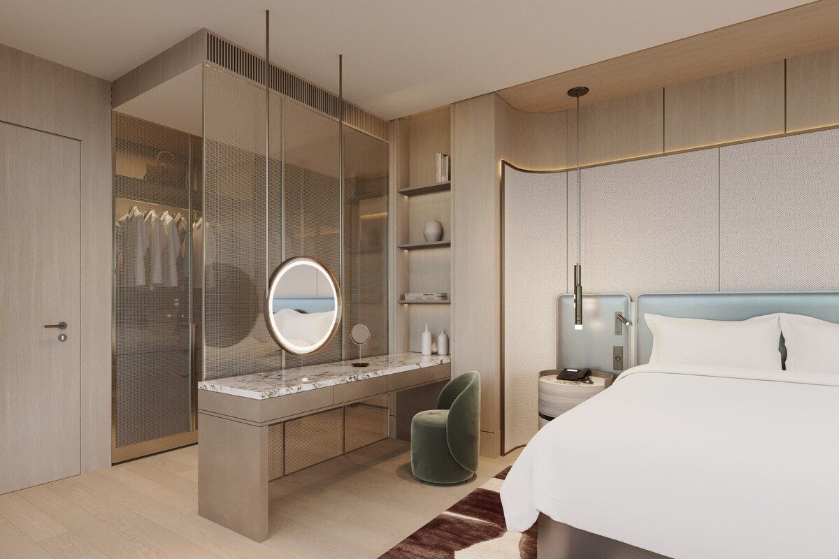 Un dormitorio moderno con una cama grande, un espejo redondo, un tocador con encimera de mármol y una silla verde.