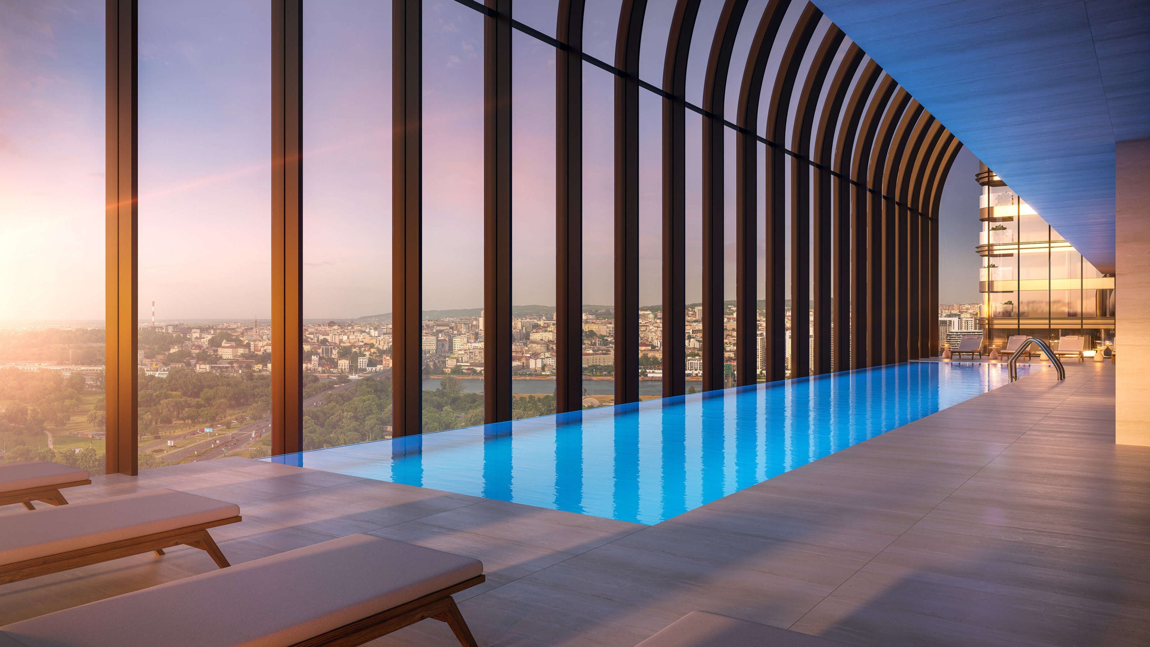 Una piscina interior moderna con vistas a la ciudad, sillones de descanso y una estructura de techo curvada.
