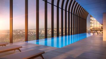 Una piscina interior moderna con vistas a la ciudad, sillones de descanso y una estructura de techo curvada.
