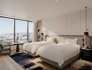 Habitación de hotel moderna con vistas a la ciudad, dos camas, un escritorio y un ventanal grande.