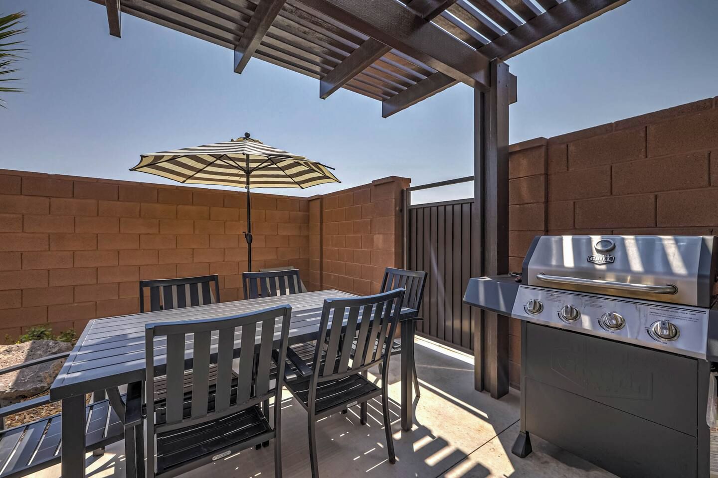 An outdoor patio with a table and chairs, a grill, and a pergola with an umbrella.