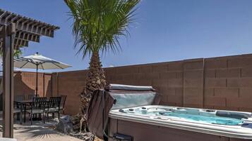 Un jacuzzi en un patio trasero con una mesa y sillas, una palmera y un muro de ladrillo.