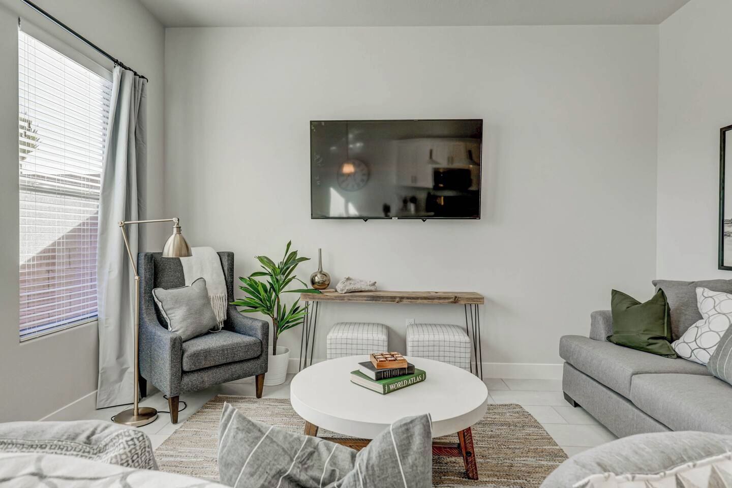 A modern living room with a grey sofa, a round coffee table, a grey armchair, a floor lamp, and a dining table with chairs.